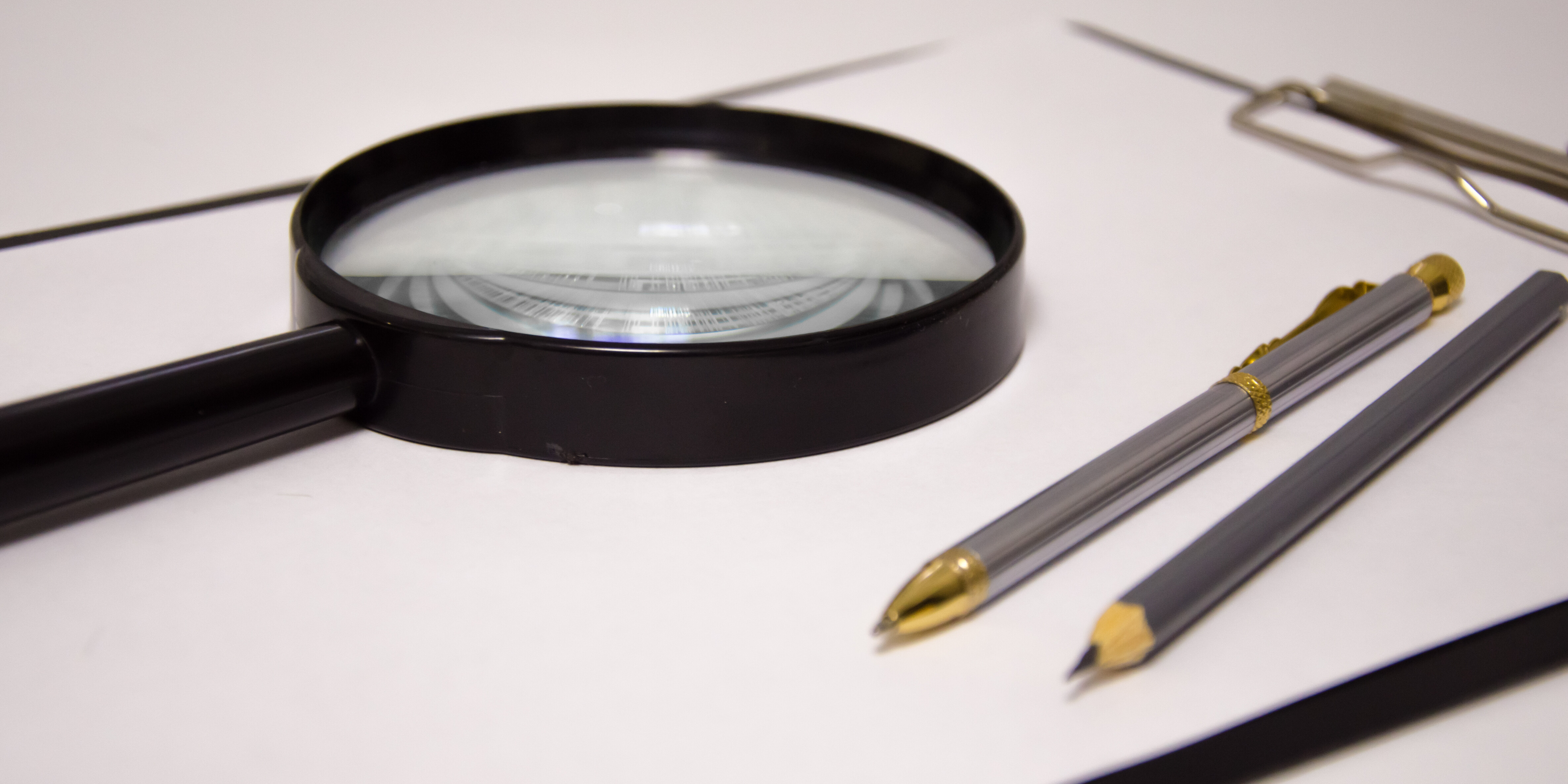 Magnifying glass and pens on clipboard Magnifying glass and pens on clipboard
